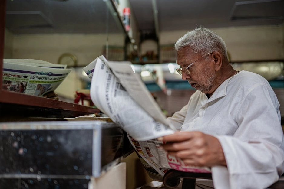 A person reading a newspaper in a quiet, well-lit cafe.
